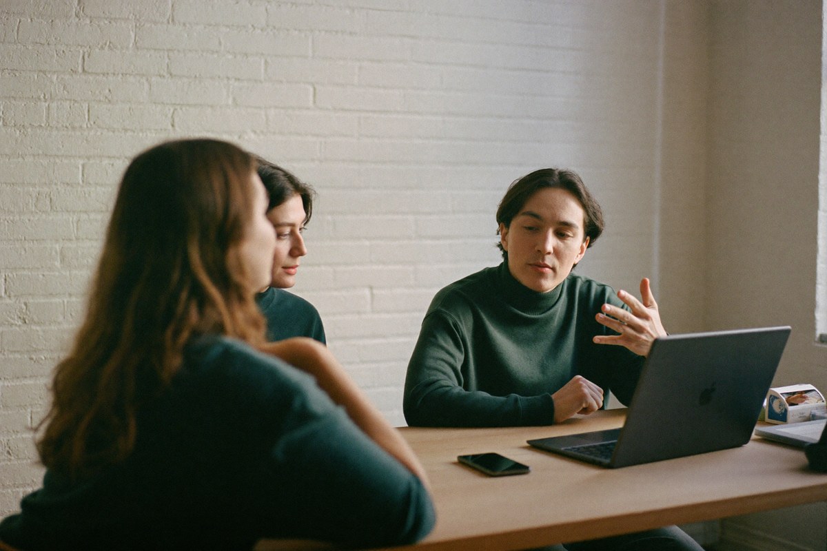 Tre persone discutono davanti a un portatile in uno studio luminoso